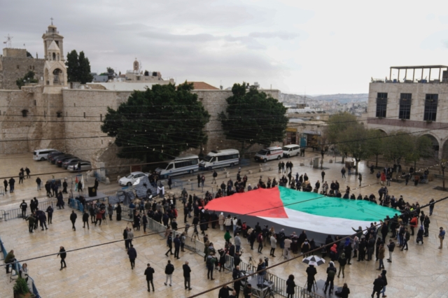 Άνθρωποι κρατούν μια γιγαντιαία παλαιστινιακή σημαία στην πλατεία Manger, κοντά στην εκκλησία της Γεννήσεως, την παραμονή των Χριστουγέννων, στην πόλη Βηθλεέμ, που παραδοσιακά θεωρείται ο τόπος γέννησης του Ιησού.