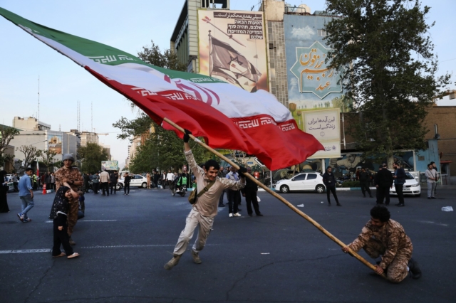 Διαδηλωτές κουνάνε μια τεράστια ιρανική σημαία στην αντι-ισραηλινή τους συγκέντρωση μπροστά από ένα αντι-ισραηλινό πανό στον τοίχο ενός κτιρίου στην πλατεία Felestin