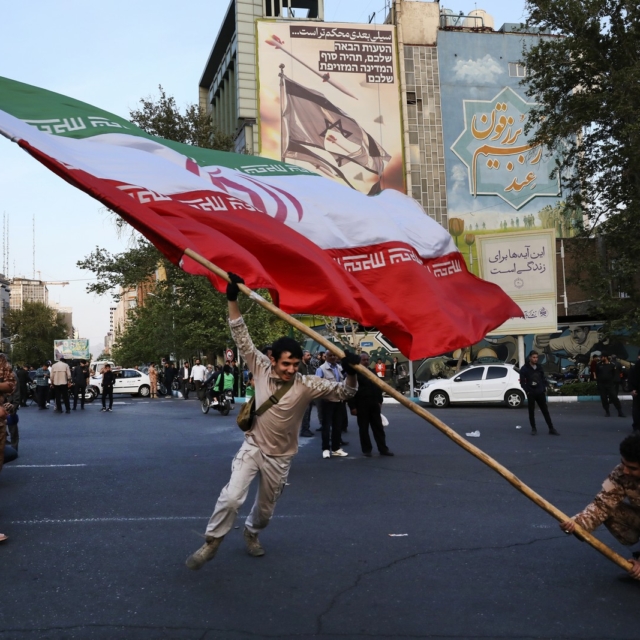 Διαδηλωτές κουνάνε μια τεράστια ιρανική σημαία στην αντι-ισραηλινή τους συγκέντρωση μπροστά από ένα αντι-ισραηλινό πανό στον τοίχο ενός κτιρίου στην πλατεία Felestin