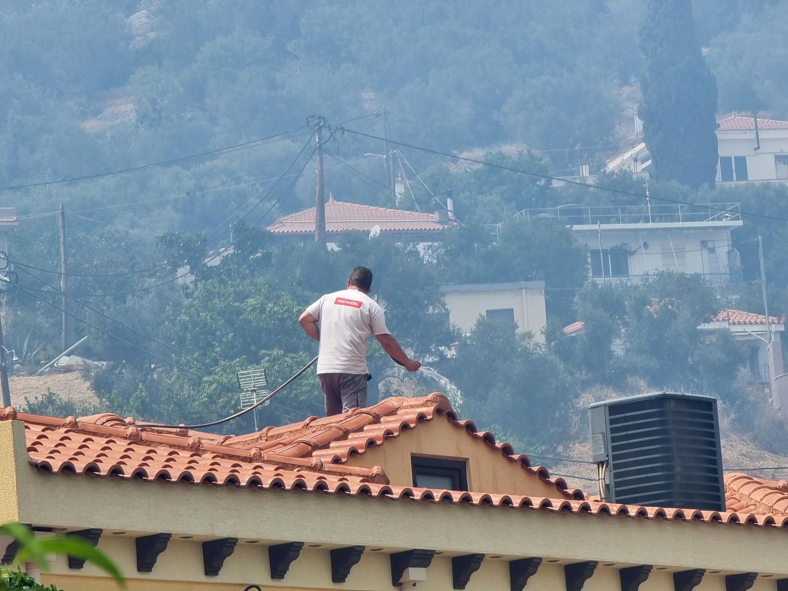 Άνδρας ρίχνει νερό στη στέγη του σπιτιού του λόγω της πυρκαγιάς που καίει δασική και θαμνώδη έκταση στην περιοχή του Τρυπατέ στις Καρυές της Χίου