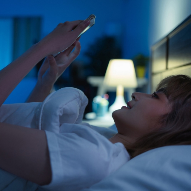Γυναίκα σκρολάρει στο κινητό της πριν κοιμηθεί
