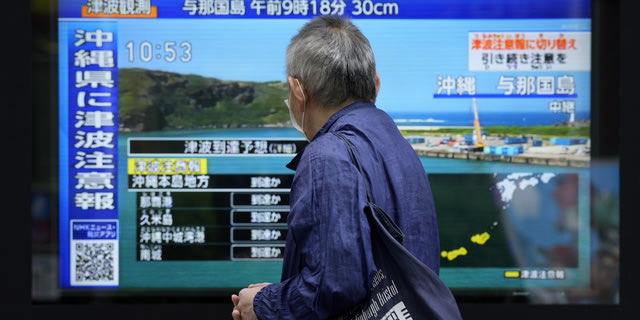 Πολίτης της Ιαπωνίας κοιτάει σε τηλεόραση στον δρόμο την προειδοποίηση για τσουνάμι