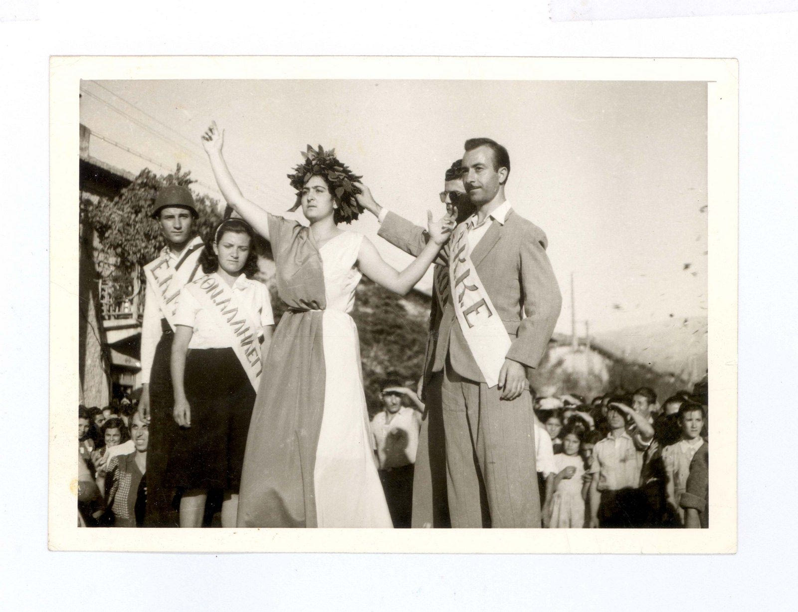 Καισαριανή 27 Σεπτεμβρίου 1944. Εορτασμός επετείου των τριών χρόνων από την ίδρυση του ΕΑΜ στην κεντρική πλατεία της Καισαριανής. Ο Θεόδωρος Κουλίτσος, συμβολίζοντας το ΚΚΕ, στεφανώνει με δάφνες κοπέλα που συμβολίζει την Ελλάδα
