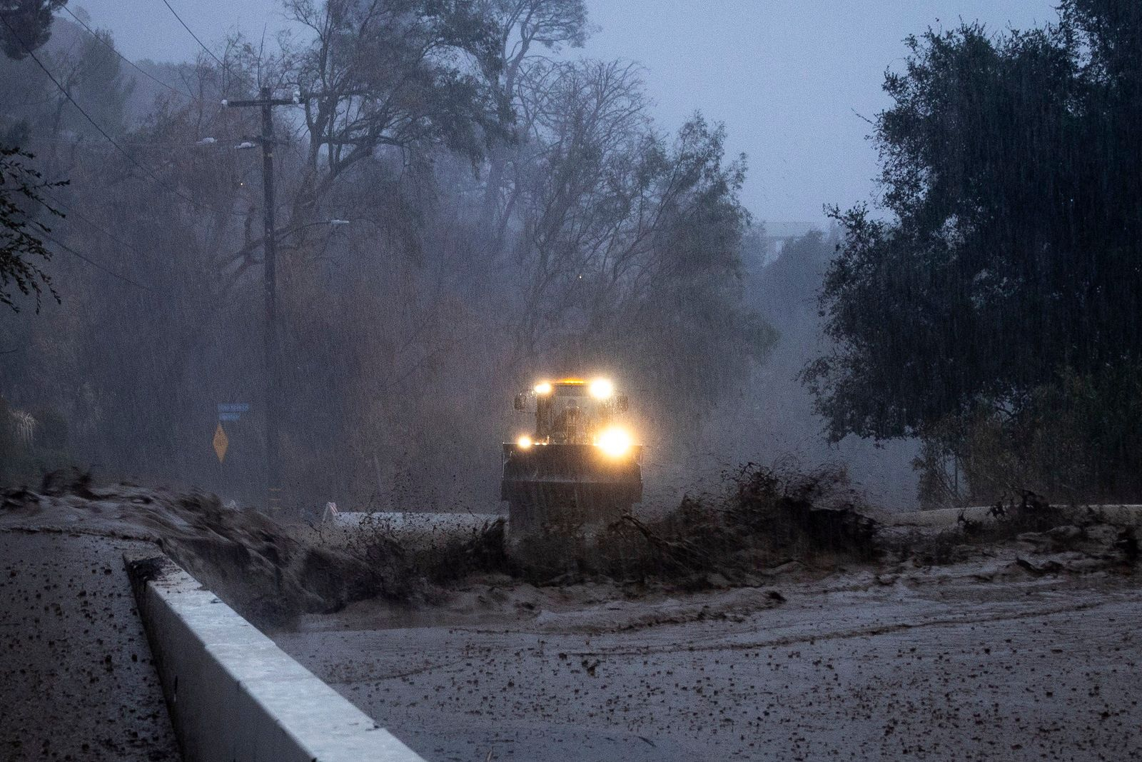 Λάσπη ρέει σε ένα δρόμο κατά τη διάρκεια μιας πλημμύρας μπροστά από μια μπουλντόζα που καθαρίζει τα συντρίμμια στη ζώνη πυρκαγιάς Eaton κατά τη διάρκεια μιας καταιγίδας την Πέμπτη, 13 Φεβρουαρίου 2025, στην Altadena της Καλιφόρνια.