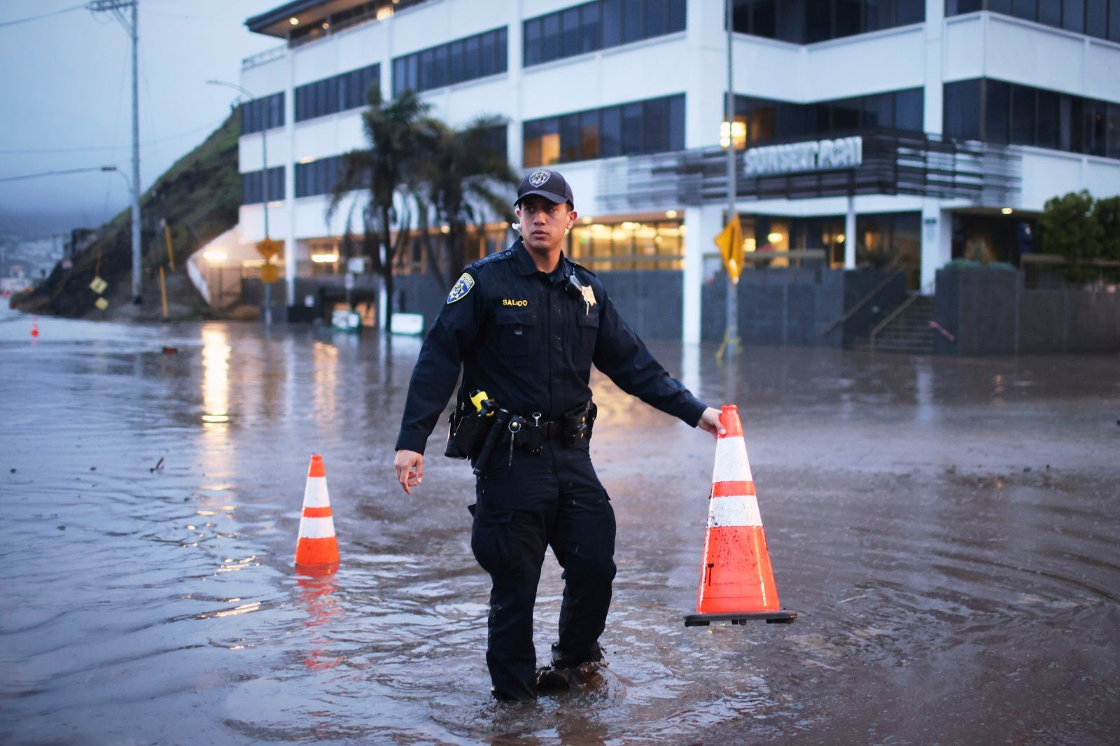 Ένας αστυνομικός στέκεται σε μια πλημμυρισμένη διασταύρωση κατά τη διάρκεια μιας καταιγίδας την Πέμπτη 13 Φεβρουαρίου 2025, στη γειτονιά Pacific Palisades του Λος Άντζελες.