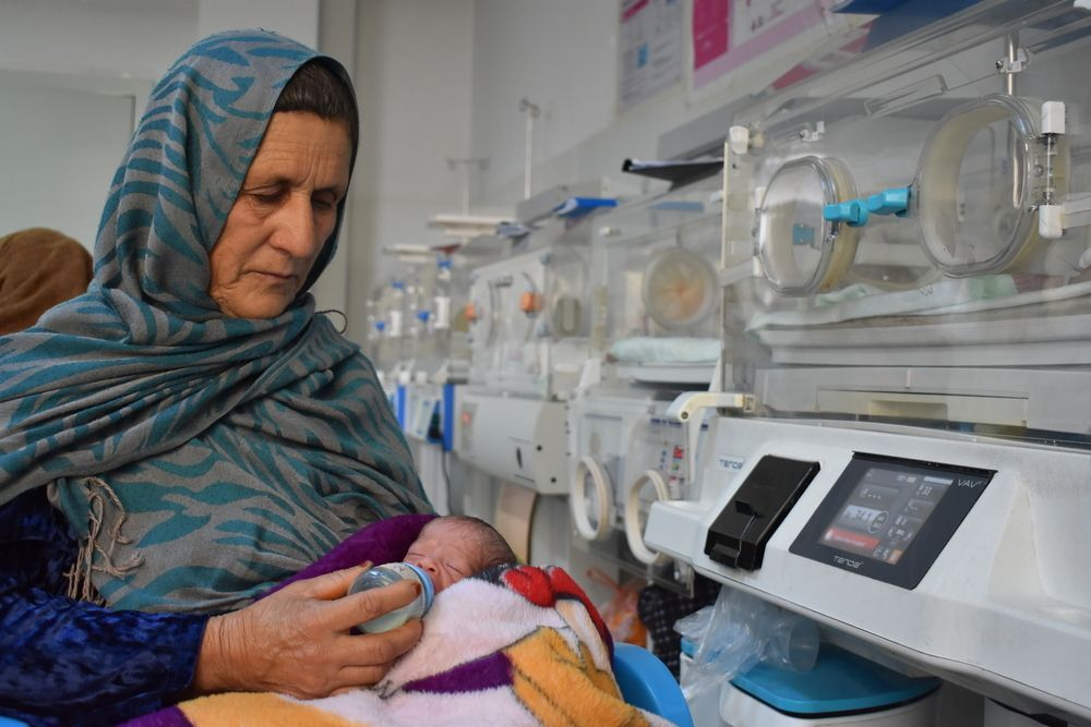 Η Reza Gul, 60 ετών, κρατάει τον πρόωρα γεννημένο εγγονό της και τον ταΐζει γάλα στον θάλαμο νεογνών του Περιφερειακού Νοσοκομείου Mazar-i-Sharif στην επαρχία Balkh που υποστηρίζεται από τους Γιατρούς Χωρίς Σύνορα. Η κόρη της γέννησε πρόωρα τρίδυμα σε μια ιδιωτική κλινική και ζύγιζαν λιγότερο από ένα κιλό το καθένα. Ο γιατρός τα παρέπεμψε στο περιφερειακό νοσοκομείο, όπου τα βρέφη παρέμειναν υπό στενή παρακολούθηση μέχρι να πάρουν αρκετό βάρος για να πάρουν εξιτήριο. Το 23 ημερών αγοράκι είναι το τελευταίο από τα αδελφάκια του που παρέμεινε στο νοσοκομείο. Οι δύο αδελφές του πήραν ήδη εξιτήριο, αφού είχαν πάρει αρκετό βάρος για να πάνε στο σπίτι τους νωρίτερα μέσα στην εβδομάδα.