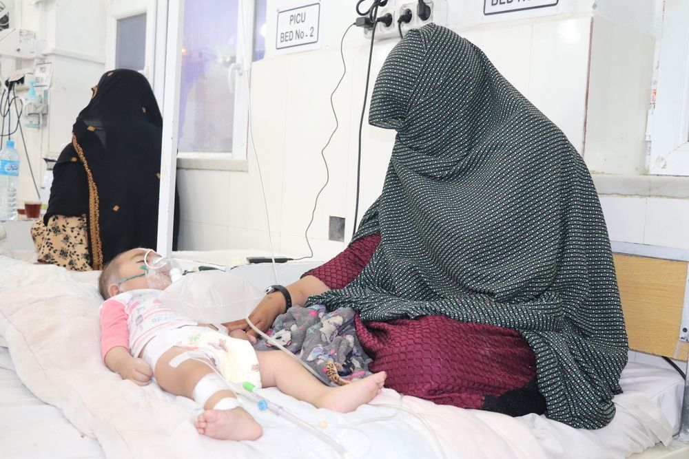 Η 20χρονη Zarmina κρατάει το χέρι της κόρης της Asma καθώς κάθεται μαζί της σε ένα κρεβάτι στη μονάδα εντατικής θεραπείας στο νοσοκομείο Boost που υποστηρίζεται από τους Γιατρούς Χωρίς Σύνορα στο Helmand. Η Asma υπέφερε από πυρετό, επιληπτικές κρίσεις, δυσκολία στην αναπνοή και δυσκαμψία στα άκρα της. Η μητέρα της την έφερε στο νοσοκομείο μετά από εβδομάδες ασθένειας. Λόγω της φτώχειας, η οικογένεια δεν μπορούσε να έχει έγκαιρη πρόσβαση στην υγειονομική περίθαλψη.