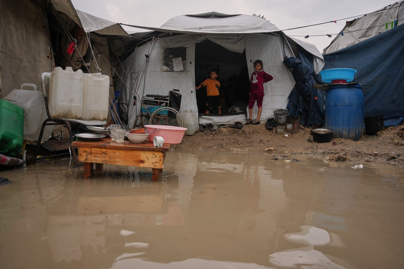 Παιδιά στέκονται στην είσοδο της σκηνής της οικογένειάς τους, δίπλα σε μια πλημμυρισμένη περιοχή, σε προσωρινό καταυλισμό για εκτοπισμένους Παλαιστίνιους μετά από έντονες βροχοπτώσεις στο Ντέιρ αλ-Μπάλαχ, στην κεντρική Λωρίδα της Γάζας, την Παρασκευή 12 Δεκεμβρίου 2025