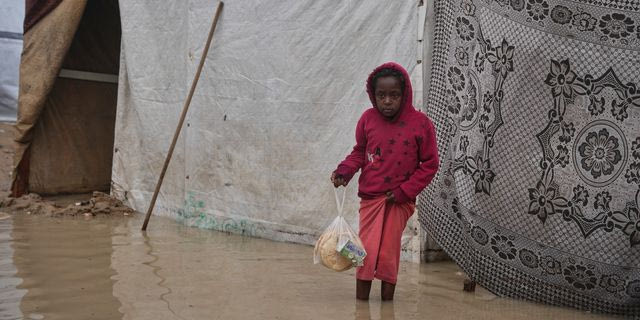 Κρατώντας μια πλαστική σακούλα με ψωμί, ο Ταχρίρ Αλ-Ραουάγ, 8 ετών, κοιτάζει γύρω του καθώς στέκεται σε μια πλημμυρισμένη περιοχή σε προσωρινό καταυλισμό σκηνών μετά από έντονες βροχοπτώσεις στο Ντέιρ αλ-Μπάλαχ, στην κεντρική Λωρίδα της Γάζας, την Παρασκευή 12 Δεκεμβρίου 2025