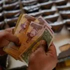 Ένας πωλητής μετράει μπολίβαρ Βενεζουέλας και χαρτονομίσματα δολαρίων ΗΠΑ για να παραδώσει ρέστα σε έναν πελάτη σε υπαίθρια αγορά στο Καράκας της Βενεζουέλας, Σάββατο, 20 Δεκεμβρίου 2025.