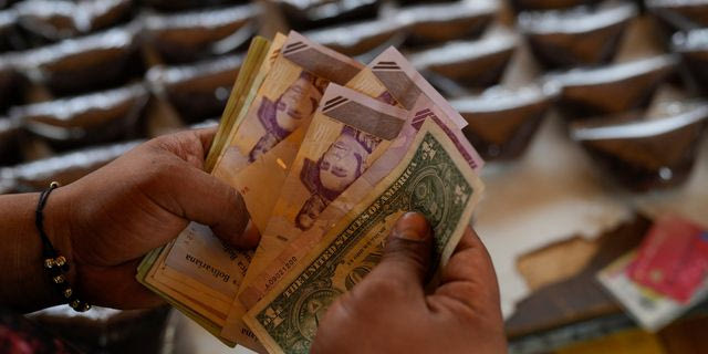 Ένας πωλητής μετράει μπολίβαρ Βενεζουέλας και χαρτονομίσματα δολαρίων ΗΠΑ για να παραδώσει ρέστα σε έναν πελάτη σε υπαίθρια αγορά στο Καράκας της Βενεζουέλας, Σάββατο, 20 Δεκεμβρίου 2025.
