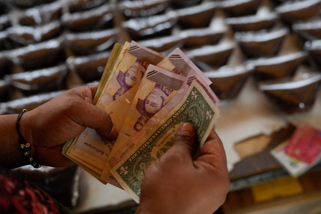 Ένας πωλητής μετράει μπολίβαρ Βενεζουέλας και χαρτονομίσματα δολαρίων ΗΠΑ για να παραδώσει ρέστα σε έναν πελάτη σε υπαίθρια αγορά στο Καράκας της Βενεζουέλας, Σάββατο, 20 Δεκεμβρίου 2025.