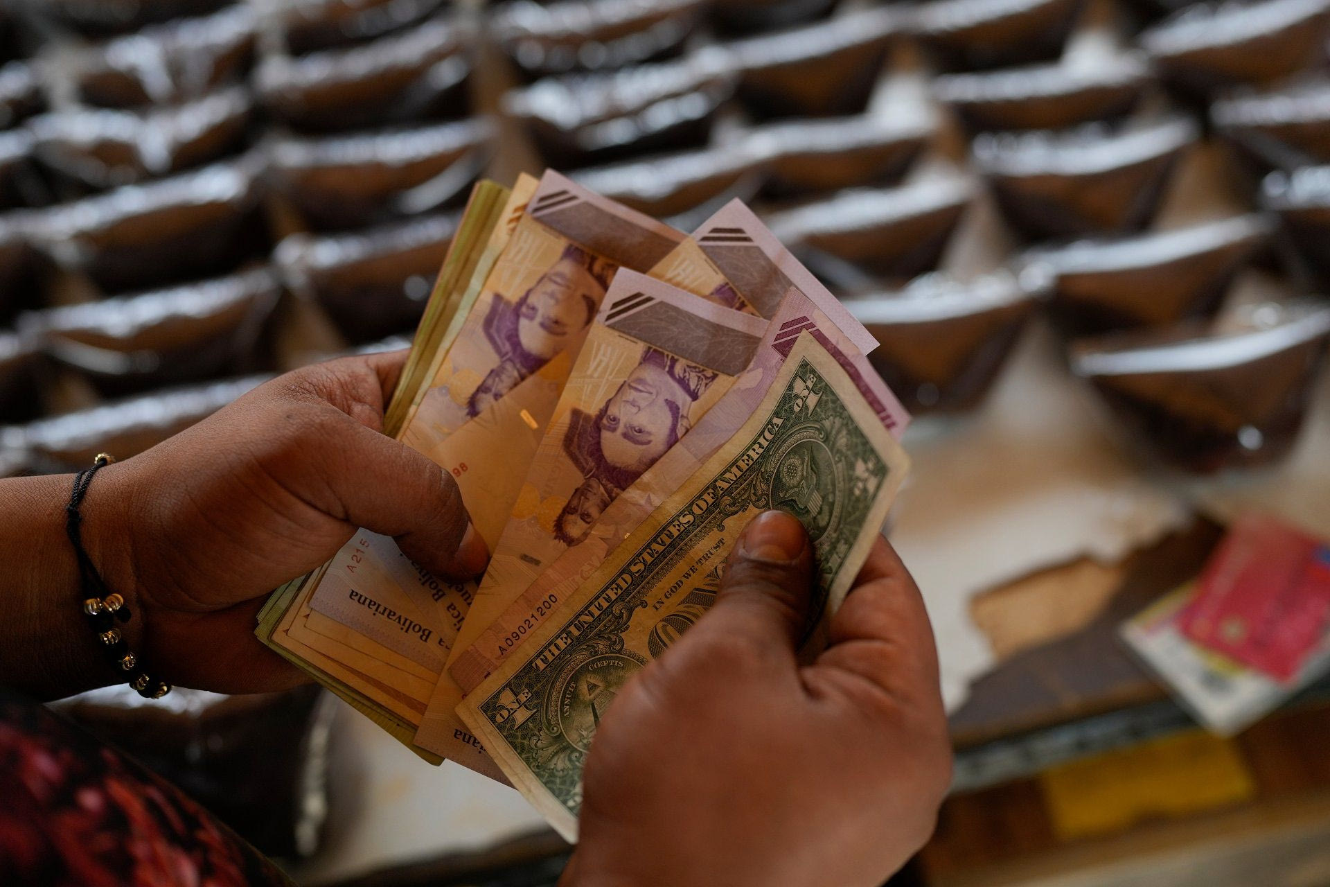 Ένας πωλητής μετράει μπολίβαρ Βενεζουέλας και χαρτονομίσματα δολαρίων ΗΠΑ για να παραδώσει ρέστα σε έναν πελάτη σε υπαίθρια αγορά στο Καράκας της Βενεζουέλας, Σάββατο, 20 Δεκεμβρίου 2025.