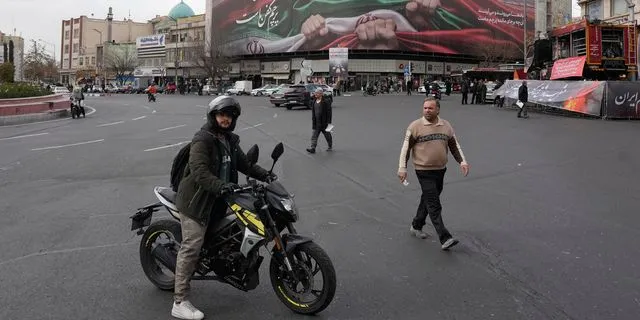 Ένας άνδρας στέκεται με τη μοτοσικλέτα του μπροστά σε ένα τεράστιο πανό που δείχνει χέρια να κρατούν ιρανικές σημαίες ως σύμβολο πατριωτισμού στην Τεχεράνη