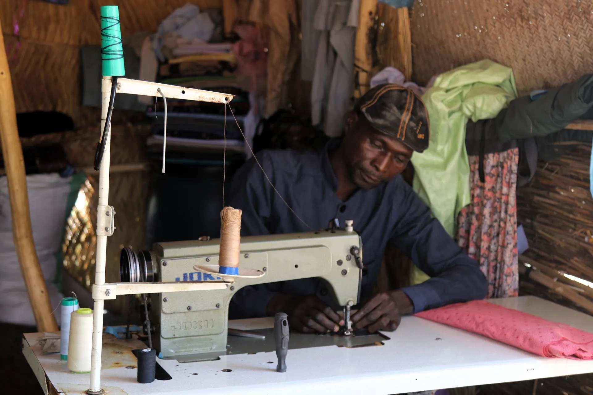 Ο Μουσταφά διέφυγε από τη γενοκτονία στο Νταρφούρ και έφτασε στον καταυλισμό Κουφράμ, φέρνοντας μαζί τη ραπτομηχανή του. Εκεί άνοιξε ένα μικρό εργαστήριο επιδιόρθωσης ρούχων