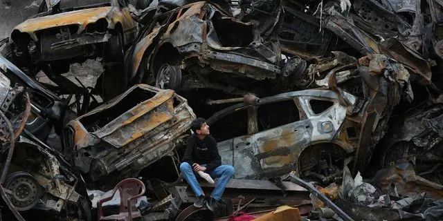 Ένας νεαρός κάθεται δίπλα σε απανθρακωμένα αυτοκίνητα και συντρίμμια στο Ιράν