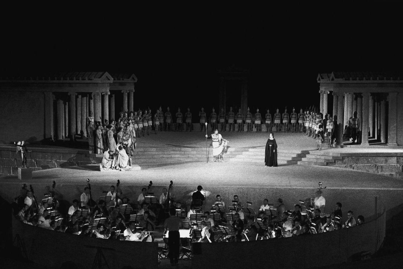 Tο Σάββατο 20 Ιουνίου 2026, στο Αρχαίο Θέατρο Επιδαύρου, η Εθνική Λυρική Σκηνή θα παρουσιάσει τη Μήδεια του Λουίτζι Κερουμπίνι, σε μουσική διεύθυνση Ζακ Λακόμπ και σκηνοθεσία Παναγή Παγουλάτου, με την Άννα Πιρότσι στον ρόλο του τίτλου. Πρόκειται για την ανασύνθεση της ιστορικής Μήδειας του 1961, που σφράγισε με την αξεπέραστη ερμηνεία της η Μαρία Κάλλας, στη σκηνοθεσία του Αλέξη Μινωτή, με σκηνικά και κοστούμια του Γιάννη Τσαρούχη και χορογραφία της Μαρίας Χορς. Τα εισιτήρια για την παράσταση, με την οποία εγκαινιάζεται το πρόγραμμα των φετινών Επιδαυρίων, έχουν εξαντληθεί από τον περασμένο Φεβρουάριο, μία εβδομάδα μετά την έναρξη της προπώλησης. Η Μήδεια του Κερουμπίνι, έργο βασισμένο στην ομώνυμη τραγωδία του Ευριπίδη, ανασύρθηκε από τη λήθη και επανήλθε στο διεθνές προσκήνιο χάρη στη Μαρία Κάλλας, η οποία ερμήνευσε για πρώτη φορά τον ρόλο του τίτλου το 1953 στο Φεστιβάλ του Φλωρεντινού Μουσικού Μάη. Η ιστορική παρουσίασή της από την Εθνική Λυρική Σκηνή στο Αρχαίο Θέατρο της Επιδαύρου το 1961, σε σκηνοθεσία Αλέξη Μινωτή, με σκηνικά και κοστούμια του Γιάννη Τσαρούχη και χορογραφία της Μαρίας Χορς, αποτέλεσε κορυφαία στιγμή της σύγχρονης ελληνικής πολιτιστικής ιστορίας και σφράγισε ανεξίτηλα τη συλλογική μνήμη. Ο Κερουμπίνι συνέθεσε τη Μήδεια στα τέλη του 18ου αιώνα σε γαλλικό ποιητικό κείμενο του Φρανσουά-Μπενουά Οφμάν. Η πρεμιέρα του έργου πραγματοποιήθηκε στο Παρίσι το 1797. Η ΕΛΣ παρουσιάζει την ιταλική εκδοχή του έργου που μεταφράστηκε από τον Κάρλο Τσανγκαρίνι, με μελοποιημένους διαλόγους του Φραντς Πάουλ Λάχνερ, ακολουθώντας την παράδοση της Κάλλας. Στον πυρήνα του έργου βρίσκεται η βαθιά ψυχογραφική προσέγγιση της Μήδειας, η οποία εμφανίζεται ως μια γυναίκα πληγωμένη, παθιασμένη και ακραία ανθρώπινη, που ακροβατεί από την απόγνωση και την ταπείνωση στην εκδικητική μανία που την οδηγεί να ξαναβρεί την υπερφυσική της πλευρά ως μάγισσας. Η Μήδεια του 1961, ένα από τα σημαντικότερα καλλιτεχνικά γεγονότα της μεταπολεμικής Ελλάδας, συνέδεσε την Εθνική Λυρική Σκηνή με τα μεγαλύτερα οπερατικά κέντρα του κόσμου. Όταν το 1958 η νεοσύστατη Όπερα του Ντάλλας αναθέτει στη Μαρία Κάλλας μια νέα παραγωγή της Μήδειας, η Divina ζητά να τη σκηνοθετήσει ο Αλέξης Μινωτής, ο Έλληνας σκηνοθέτης που συνδέθηκε όσο κανείς με την αρχαία ελληνική τραγωδία. Παρά τους αρχικούς δισταγμούς του, λόγω της απειρίας του στο λυρικό θέατρο, και μετά την επιμονή της Κατίνας Παξινού, ο Μινωτής δέχεται και προτείνει ως σκηνογράφο και ενδυματολόγο τον κορυφαίο Έλληνα ζωγράφο Γιάννη Τσαρούχη. Η πρεμιέρα στο Ντάλλας στέφεται από μια χωρίς προηγούμενο επιτυχία, με τις διθυραμβικές κριτικές να αναφέρονται σε μια «υπερφυσική αλλά ταυτόχρονα ανθρώπινη Κάλλας», στον «ανανεωτικό αέρα της σκηνοθεσίας του Μινωτή» και στα «130 φτιαγμένα στην Ελλάδα, μοναδικά κοστούμια του Τσαρούχη». Η παραγωγή, μετά την πρώτη της παρουσίαση στην Όπερα του Ντάλλας, παρουσιάστηκε το 1959 στη Βασιλική Όπερα του Λονδίνου, συνέχισε το καλοκαίρι του 1961 στο Αρχαίο Θέατρο της Επιδαύρου και ολοκλήρωσε τη θριαμβευτική της πορεία το 1962 στη Σκάλα του Μιλάνου. Για τον ανοιχτό χώρο της Επιδαύρου ο Μινωτής επαναπροσδιορίζει τους σκηνοθετικούς χειρισμούς, θέλοντας, όπως ο ίδιος έχει επισημάνει, να «επαναφέρει όσο μπορούσε την λειτουργία του μύθου κατά το αρχαίο πρότυπο, χωρίς να παραβλάψει στο ελάχιστο την μουσική του διάσημου συνθέτη». Παράλληλα ο Τσαρούχης σχεδιάζει νέο σκηνικό ειδικά για το αρχαίο θέατρο, ενώ δημιουργεί νέα κοστούμια για τα συνολικά 250 άτομα που βρίσκονται επί σκηνής. Στο επίκεντρο βρέθηκε η συγκλονιστική ερμηνεία της Μαρίας Κάλλας, η οποία αποθεώθηκε για τη δραματική ένταση, τη θεατρικότητα και τη μοναδική εκφραστικότητα της φωνής της, επιβεβαιώνοντας τον μύθο της ως της κορυφαίας λυρικής τραγουδίστριας του 20ού αιώνα. Η παραγωγή έμεινε στην ιστορία ως ένας προσωπικός θρίαμβος της Κάλλας, αλλά και ως ένα εμβληματικό καλλιτεχνικό επίτευγμα που ανέδειξε διεθνώς την ελληνική δημιουργία και άφησε ανεξίτηλο αποτύπωμα στη συλλογική μνήμη. Εξήντα πέντε χρόνια μετά, η Εθνική Λυρική Σκηνή φωτίζει ξανά την ιστορική παράσταση, στο πλαίσιο του θεματικού άξονα της καλλιτεχνικής περιόδου 2025/26 «Η όπερα του μέλλοντος μέσα από τη μήτρα του παρελθόντος», σε καλλιτεχνική διεύθυνση Γιώργου Κουμεντάκη. Μέσα από τα τετράδια σκηνοθεσίας του Μινωτή, τα σχέδια του Τσαρούχη, καθώς και το φωτογραφικό υλικό που σώζεται από τις πρόβες και τις παραστάσεις στην Επίδαυρο, δημιουργείται μια ανασύνθεση της παραγωγής του 1961, όπως την εμπνεύστηκαν και την παρουσίασαν οι μυθικοί εκείνοι καλλιτέχνες που σφράγισαν τον ελληνικό πολιτισμό. Ο Παναγής Παγουλάτος, με μεγάλη εμπειρία στη σκηνοθεσία της όπερας και πολυετή μελέτη της επίδρασης της Κάλλας στη λυρική τέχνη, υπογράφει τη σκηνοθεσία. Βάση της εργασίας του αποτέλεσε η συστηματική μελέτη αρχειακού υλικού – φωτογραφιών, σκηνοθετικών σημειώσεων, σπαρτίτο, κοστουμιών και αλληλογραφίας της εποχής. Προσεγγίζοντας το έργο με βαθύ σεβασμό απέναντι στη μουσική δραματουργία του Κερουμπίνι, αλλά ταυτόχρονα και στην παράδοση της αρχαίας τραγωδίας και στη θεατρική γλώσσα του Μινωτή, επιλέγει μια σκηνική απόδοση λιτή και αυστηρή, ακολουθώντας το γράμμα και το πνεύμα της ιστορικής παράστασης του 1961. Ο σκηνοθέτης σημειώνει: «Ο Αλέξης Μινωτής ήταν ένας θεατρικός σκηνοθέτης που ασχολήθηκε κατεξοχήν με την αρχαία τραγωδία. Από τα σκηνικά, τα κοστούμια, τις φωτογραφίες και τις σημειώσεις του επιβεβαιώνουμε ότι η σκηνοθεσία του είναι πιστή στο λιμπρέτο. Ο ίδιος έχει ακολουθήσει τις οδηγίες του κειμένου, αλλά και του συνθέτη, με μια συγκεκριμένη λογική. Δεν έχει κάνει κάτι αντίθετο στο κείμενο, ούτε κάτι εικονοκλαστικό για τα σύγχρονα κριτήρια. Το επαναστατικό εκείνη την εποχή ήταν η ίδια η Κάλλας, που ήταν η πρώτη άδουσα τραγωδός με όλη τη βαρύτητα της λέξης. Μέσα στο ίδιο πνεύμα κινείται και η δική μου σκηνοθεσία. Δεν την ανέλαβα για να εκθέσω την προσωπική μου άποψη για τη Μήδεια, αλλά για να υπηρετήσω ένα συγκεκριμένο όραμα, εκείνο του 1961. Φυσικά έχουν γίνει πολλές προσαρμογές ανάλογα με τις διαφοροποιήσεις του σκηνικού, τις προσωπικότητες των καλλιτεχνών, τη σύγχρονη αντίληψη ερμηνείας». Η διακεκριμένη σκηνογράφος και καθηγήτρια σκηνογραφίας στην Ανώτατη Σχολή Καλών Τεχνών Λίλη Πεζανού μελέτησε τις φωτογραφίες από τις μακέτες του σκηνικού του Γιάννη Τσαρούχη, τις φωτογραφίες από τις πρόβες και την παράσταση του 1961, καθώς και τη σωζόμενη αλληλογραφία, με στόχο να ανασυνθέσει τα –εμπνευσμένα από την ελληνιστική αρχαιότητα– σκηνικά της παραγωγής, τα οποία έχουν προσαρμοστεί στον τρόπο που σήμερα στήνονται οι παραστάσεις στο Αρχαίο Θέατρο της Επιδαύρου. Η ενδυματολόγος του θεάτρου, της όπερας και του κινηματογράφου Τότα Πρίτσα, ξεκινώντας από τα αυθεντικά κοστούμια της παραγωγής που σώζονται στο Βεστιάριο της ΕΛΣ, έκανε μια μεγάλη έρευνα αναφορικά με τις υφές, τις αποχρώσεις, την ελαστικότητα, τη ρευστότητα, ακόμα και την απόδοση των πτυχώσεων των υφασμάτων των κοστουμιών, για την ανασύνθεση της παραγωγής. Υπηρετώντας τον στόχο του Τσαρούχη –ο οποίος θεωρούσε κρίσιμο «τα κοστούμια να προσεγγίζουν τη φυσική κίνηση του σώματος και τη γλυπτική ποιότητα της αρχαιοελληνικής ενδυμασίας»– η έμπειρη ενδυματολόγος έκανε προσαρμογές όπου κρίθηκε αναγκαίο χωρίς όμως ποτέ να αλλοιώνεται η βασική αισθητική του κατεύθυνση. Όπως χαρακτηριστικά αναφέρει στο σημείωμα για την εργασία της πάνω στον Τσαρούχη: «Εδώ το ένδυμα δεν περιγράφει μια εποχή· κρατά μια μνήμη. Και η σκηνή δεν αναπαριστά – συνθέτει. Σαν να άπλωσε ο ίδιος ο ζωγράφος τα χρώματά του πάνω στο σώμα του ηθοποιού, και το άφησε να κινηθεί». Οι διεθνώς αναγνωρισμένες χορογράφοι Γιάννα Φιλιπποπούλου και Κέλλη Ζαμπέλα αναβιώνουν τη χορογραφία της Μαρίας Χορς, βάσει των σημειώσεων και των οδηγιών που υπάρχουν στο βιβλίο σκηνοθεσίας, ενώ ο Χρήστος Τζιόγκας υπογράφει τους φωτισμούς της παραγωγής αναμετρώμενος με τη μεγάλη πρόκληση της ανασύνθεσης της ατμόσφαιρας της παράστασης του 1961. Την Ορχήστρα της Εθνικής Λυρικής Σκηνής διευθύνει ο διεθνώς καταξιωμένος αρχιμουσικός Ζακ Λακόμπ, στην τέταρτη συνεργασία του με την ΕΛΣ, μετά την Μποέμ, τον Βέρθερο και την Άννα Μπολένα που παρουσιάστηκε τη φετινή σεζόν. Ο Λακόμπ έχει διατελέσει στο παρελθόν αρχιμουσικός της Όπερας της Βόννης, μουσικός διευθυντής της Συμφωνικής Ορχήστρας του Νιου Τζέρσεϋ, καθώς και της Συμφωνικής Ορχήστρας της Μυλούζης. Έχει συνεργαστεί με πολλές σπουδαίες όπερες, όπως τη Βασιλική Όπερα Λονδίνου, τη Μετροπόλιταν της Νέας Υόρκης, τη Γερμανική Όπερα Βερολίνου, την Κρατική Όπερα Βαυαρίας. Τη Χορωδία της ΕΛΣ έχει προετοιμάσει ο Αγαθάγγελος Γεωργακάτος. Για την ανασύνθεση της ιστορικής παραγωγής του 1961, η Εθνική Λυρική Σκηνή έχει εξασφαλίσει ένα εξαιρετικό καστ διεθνούς ακτινοβολίας, σε συνδυασμό με σημαντικούς λυρικούς τραγουδιστές της ελληνικής οπερατικής σκηνής. Τον ρόλο του τίτλου θα ερμηνεύσει η σπουδαία Ιταλίδα δραματική υψίφωνος Άννα Πιρότσι, η οποία έκανε το ντεμπούτο της στον ρόλο στην παραγωγή της ΕΛΣ το 2023 σε σκηνοθεσία του Ντέιβιντ ΜακΒίκαρ, με διθυραμβικές κριτικές για την ερμηνεία της. Η Πιρότσι, την οποία το ελληνικό κοινό χειροκρότησε θερμά στον ρόλο της Τζοκόντας τον περασμένο Οκτώβριο στην ΕΛΣ, έχει διαγράψει μια μοναδική σταδιοδρομία μετά το ντεμπούτο της στο Τορίνο το 2012 και την τεράστια επιτυχία που σημείωσε στο Φεστιβάλ του Ζάλτσμπουργκ ως Αμπιγκαΐλλε σε διεύθυνση του Ρικκάρντο Μούτι. Πρωταγωνιστεί στις μεγαλύτερες όπερες του πλανήτη, όπως, μεταξύ άλλων, στη Βασιλική Όπερα του Λονδίνου, τη Μετροπόλιταν της Νέας Υόρκης, τη Σκάλα του Μιλάνου, την Εθνική Όπερα του Παρισιού, την Κρατική Όπερα της Βιέννης, το Ρεάλ της Μαδρίτης. Τον ρόλο του Ιάσονα θα ερμηνεύσει ο διακεκριμένος Γάλλος τενόρος Ζαν-Φρανσουά Μπορράς. Έχει εμφανιστεί στις κορυφαίες όπερες του κόσμου, όπως στη Μετροπόλιταν της Νέας Υόρκης, στην Κρατική Όπερα του Παρισιού, στη Βιέννη, στο Λονδίνο, το Μόναχο, τη Φλωρεντία, τη Βενετία κ.α. Στην ΕΛΣ ερμήνευσε Δούκα της Μάντοβας το 2008/09 και Βέρθερο το 2013/14. Στον ρόλο του Κρέοντα θα ντεμπουτάρει ο Τάσης Χριστογιαννόπουλος, καταξιωμένος πρωταγωνιστής της Εθνικής Λυρικής Σκηνής και Καλλιτεχνικός Διευθυντής του Ολύμπια Δημοτικού Μουσικού Θεάτρου «Μαρία Κάλλας». Ο Χριστογιαννόπουλος πρωταγωνιστεί από το 1989 σε παραγωγές της ΕΛΣ, ενώ εμφανίζεται τακτικά στα σημαντικότερα θέατρα παγκοσμίως, όπως, μεταξύ άλλων, σε Οπερά Κομίκ, Εθνική Όπερα Παρισιού, Θέατρο Ηλυσίων Πεδίων στο Παρίσι, Βασιλική Όπερα Λονδίνου. Η γνώριμη στο ελληνικό κοινό από τη Μαντάμα Μπαττερφλάι (Σουτζούκι) του 2023 και την Τζοκόντα (Λάουρα) του 2025 Αλίσα Κολόσοβα θα ερμηνεύσει τον ρόλο της Νέριδας. Η κορυφαία Ρωσίδα μεσόφωνος εμφανίζεται τακτικά στις σημαντικότερες όπερες και φεστιβάλ της Ευρώπης και της Αμερικής, όπως, μεταξύ άλλων, σε Παρίσι, Μιλάνο, Μόναχο, Βερολίνο, Βιέννη, Ζάλτσμπουργκ, Πέζαρο, Γκλάιντμπορν. Τη Γλαύκη θα ερμηνεύσει η κολορατούρα υψίφωνος Δανάη Κοντόρα, η οποία έχει διαγράψει ήδη μια πολύ σημαντική πορεία παγκοσμίως. Έχει εμφανιστεί, μεταξύ άλλων, σε Βερολίνο, Παρίσι, Βιέννη, Αμβούργο, Φρανκφούρτη, Πεκίνο, Ταϊβάν, Λονδίνο. Στους ρόλους του επικεφαλής της φρουράς και των δύο υπηρετριών οι Γιάννης Σταματάκης, Αιμιλία Τσιμιδάκη και Ειρήνη Αθανασίου. > Με αφορμή την ανασύνθεση της ιστορικής Μήδειας του 1961 στο Αρχαίο Θέατρο της Επιδαύρου, η Εθνική Λυρική Σκηνή παρουσιάζει την έκθεση Σημείο Κάλλας στον περιβάλλοντα χώρο του Αρχαίου Θεάτρου Επιδαύρου, από τις 18 έως και τις 21 Ιουνίου 2026, με την υποστήριξη της ΔΕΗ. Την επιμέλεια της έκθεσης υπογράφει ο κορυφαίος, διεθνής Έλληνας σκηνογράφος Διονύσης Φωτόπουλος, ενώ το video art και τη βιντεοεγκατάσταση δημιουργεί ο εικαστικός και video designer Παντελής Μάκκας. Η έκθεση, με ελεύθερη είσοδο για το κοινό, θα ανοίξει για το κοινό την Πέμπτη 18 Ιουνίου στις 08.00 και θα παραμείνει επισκέψιμη έως και την Κυριακή 21 Ιουνίου στις 20.00. Πληροφορίες εδώ. Όπερα • Νέα παραγωγή • Ανασύνθεση ιστορικής παράστασης 1961 Μήδεια Λουίτζι Κερουμπίνι 20 Ιουνίου 2026 Ώρα έναρξης: 21.00 Μια νέα παραγωγή της Εθνικής Λυρικής Σκηνής, στο πλαίσιο του Φεστιβάλ Αθηνών Επιδαύρου Ιστορική παράσταση 1961 Σκηνοθεσία: Αλέξης Μινωτής Σκηνικά, κοστούμια: Γιάννης Τσαρούχης Χορογραφία: Μαρία Χορς Ανασύνθεση ιστορικής παράστασης 1961 Καλλιτεχνική διεύθυνση: Γιώργος Κουμεντάκης Μουσική διεύθυνση: Ζακ Λακόμπ Σκηνοθεσία: Παναγής Παγουλάτος Σκηνικά: Λίλη Πεζανού Κοστούμια: Τότα Πρίτσα Χορογραφία: Γιάννα Φιλιπποπούλου, Κέλλη Ζαμπέλα Φωτισμοί: Χρήστος Τζιόγκας Διεύθυνση χορωδίας: Αγαθάγγελος Γεωργακάτος Μήδεια: Άννα Πιρότσι Γλαύκη: Δανάη Κοντόρα Νέρις: Αλίσα Κολόσοβα Ιάσων: Ζαν-Φρανσουά Μπορράς Κρέων: Τάσης Χριστογιαννόπουλος Επικεφαλής της φρουράς: Γιάννης Σταματάκης Πρώτη υπηρέτρια: Αιμιλία Τσιμιδάκη Δεύτερη υπηρέτρια: Ειρήνη Αθανασίου Με την Ορχήστρα και τη Χορωδία της Εθνικής Λυρικής Σκηνής Τα εισιτήρια έχουν εξαντληθεί.